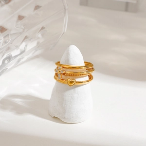 Detail of four-piece gold stackable rings featuring heart and cross charms on a stand