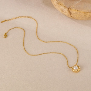 Detailed view of gold horseshoe pendant necklace with pearl on textured background