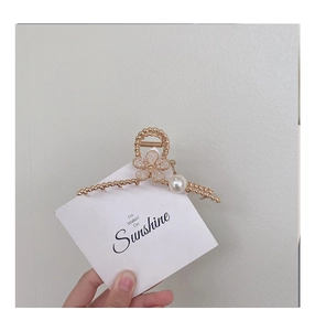 Detail of golden metal flower hair claw clip with rhinestones and a pearl pendant charm