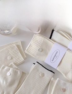 Close-up of off-white ribbed cotton socks featuring white decorative buttons and tag