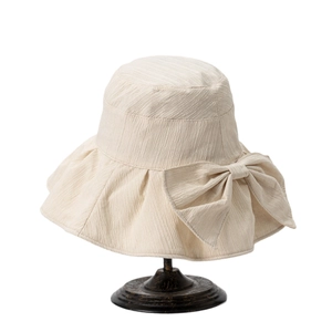 Women's cream sun hat with wide brim and large bow decoration on a vintage hat stand
