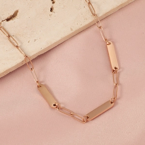 Detail shot of rose gold bar pendant and paperclip chain on beige stone and silk