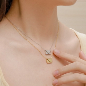 Close-up of gold and silver envelope pendants with heart detail on a delicate chain