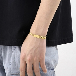 Detail of a men's gold Cuban link bracelet with a rectangular plate on a model's wrist