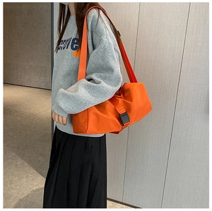 Detail of orange nylon crossbody bag with adjustable wide strap shown on a model