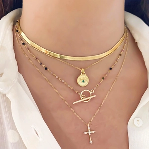 Layered gold necklaces with evil eye, green zircon coin, and cross pendant on model
