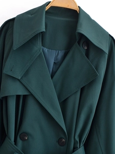 Detail of dark green trench coat featuring double-breasted resin buttons and twill texture