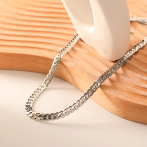 Polished silver stainless steel snake chain necklace on white ceramic and wood base