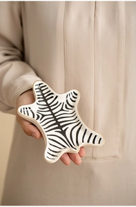 Detail of zebra pattern ceramic jewelry tray with gold trim held by hand for display