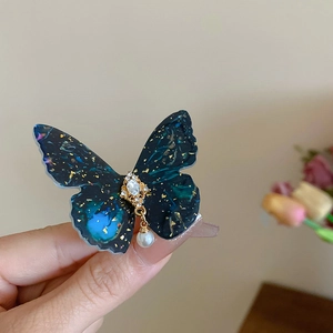 Détail de la pince papillon en acrylique bleu vert avec feuille d'or et perle