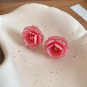 Gros plan de boucles d'oreilles fleurs en résine rose avec perle dorée sur plateau