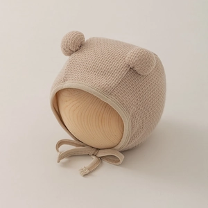 Detailed close-up of baby knit earflap hat with dual pom-poms and secure chin ties