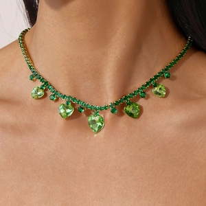 Detail of model wearing a vintage gold necklace with green heart pendant and sparkling zircons