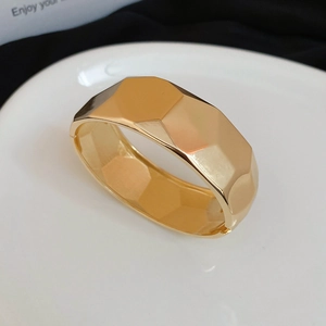 Detailed view of wide gold geometric bangle with mirror-polished facets and side hinge