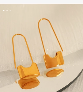 Close-up of gold padlock earrings with U-shaped clasp on white textured fabric