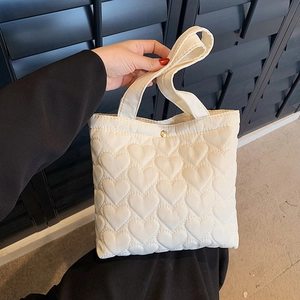 White quilted tote bag with heart pattern and golden magnetic buckle in hand
