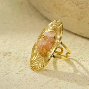 Detail of gold oval rippled ring featuring pink natural stones on a stone background