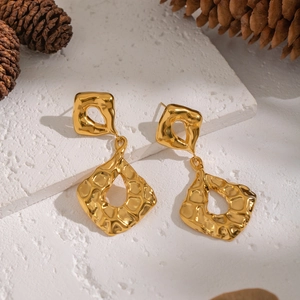 Macro detail of golden hammered geometric earrings on a natural stone background