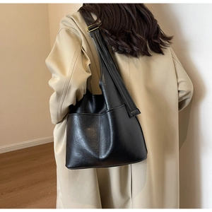 Detail einer großen schwarzen Leder-Eimertasche, getragen von einem Modell im Trenchcoat