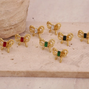 Gros plan de boucles d'oreilles nœuds dorés avec pierres précieuses sur plaque de pierre
