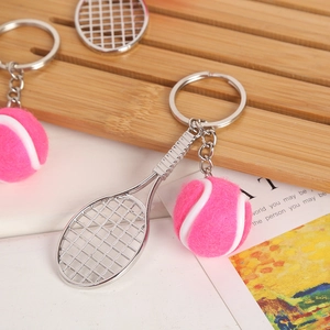 Close-up of a pink felt mini tennis ball and silver metal racket keychain on a magazine