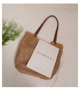 Detail of hollow woven cotton mesh shoulder bag with brown leather straps on textured fabric