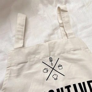 Detail of off-white canvas apron featuring black kitchen icons and POSITIVE lettering