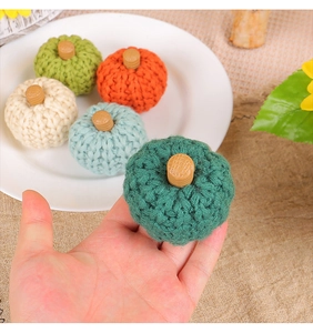 Close-up of hand holding a handmade dark green knitted pumpkin with a wooden stem