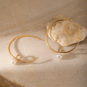Detail showing gold twisted hoop earrings with white pearls on a textured stone surface