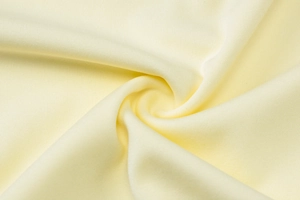 Detailed close-up of pale yellow lace dress fabric with soft knit texture and drape