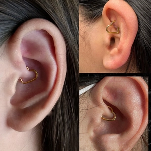 Close-up view of golden heart-shaped 316L stainless steel piercing on the daith ear area