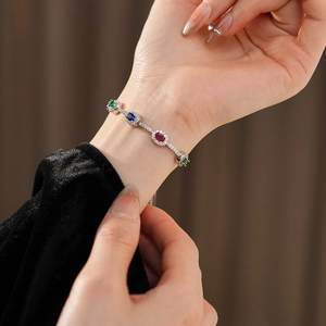 Detailansicht eines Silberarmbands mit bunten ovalen Steinen am Handgelenk auf Seide
