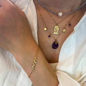 Close-up of stacked gold necklaces with purple gemstones and pearls on a model