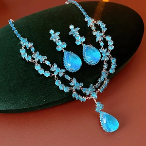 Gros plan sur l'ensemble collier et boucles d'oreilles en zircon bleu sur velours vert