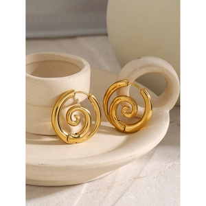 Détail de boucles d'oreilles spirales dorées sur un plateau en céramique blanche épuré