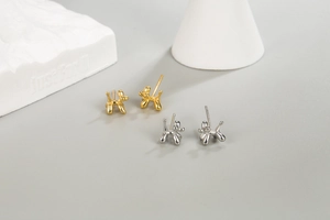 Macro detail of minimalist silver and gold balloon dog stud earrings on stone props