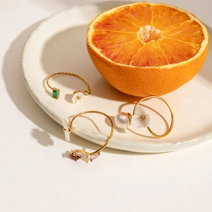 Detailed shot of 18K gold stainless steel rings with pearl and floral gems on a ceramic tray