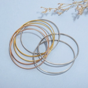 Polished stainless steel bangle set in silver, gold, and rose gold stacked on blue texture