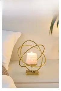 Detail of gold geometric iron candle holder with a white pillar candle on a table