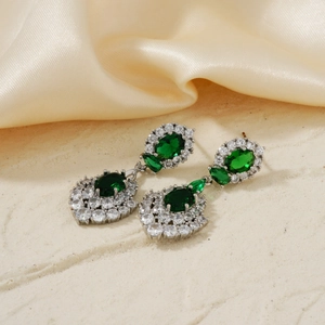 Exaggerated silver dangle earrings with green oval gemstones and white diamond accents
