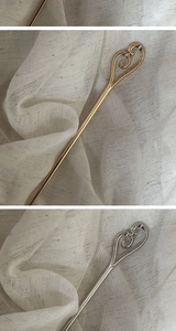 Detailed view of gold and silver metal hairpins with heart cutout on beige fabric