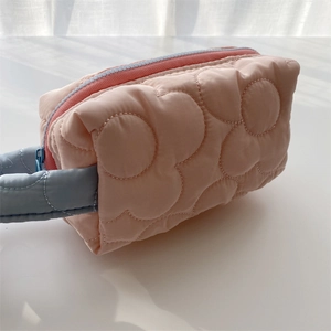 Detail of pink quilted makeup bag featuring large floral patterns and blue handle