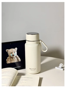 Detailed close-up of cream stainless steel vacuum flask with metal rim lid and silicone strap