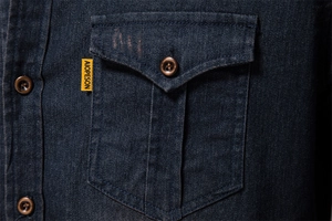 Close-up of dark blue denim shirt pocket with button flap and yellow brand label