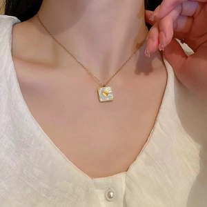 Close-up of a gold square pendant with mother of pearl and heart on a model wearing a white shirt