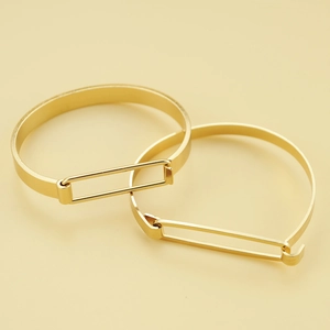Bracciali rigidi in metallo dorato con finitura lucida su uno sfondo giallo minimalista