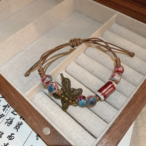Detail of vintage ceramic beaded bracelet with bronze butterfly charm and woven cord