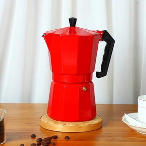 Close-up of a red aluminum moka pot on a bamboo coaster with roasted coffee beans