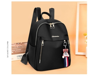 Detail of black oxford backpack with gold zippers, side pockets, and a cute bear charm