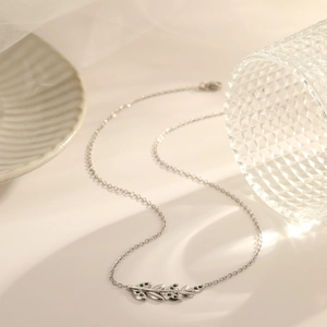 Silver leaf pendant necklace with green stones on elegant ceramic background